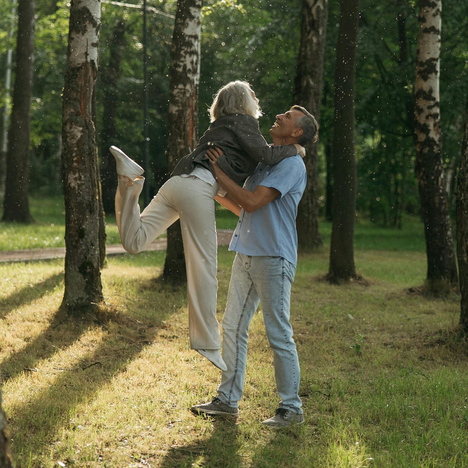 A senior man and woman sharing a hug surrounded by trees.