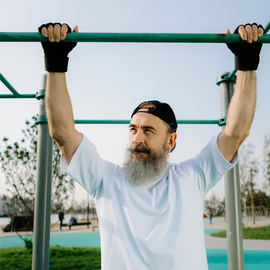 Bearded man in white shirt exercising on park bar with pull ups.