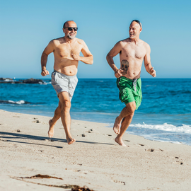 Two men sprinting along the sandy beach, with waves crashing in the background.