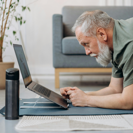 A mature man with a beard and gray hair working on a laptop.